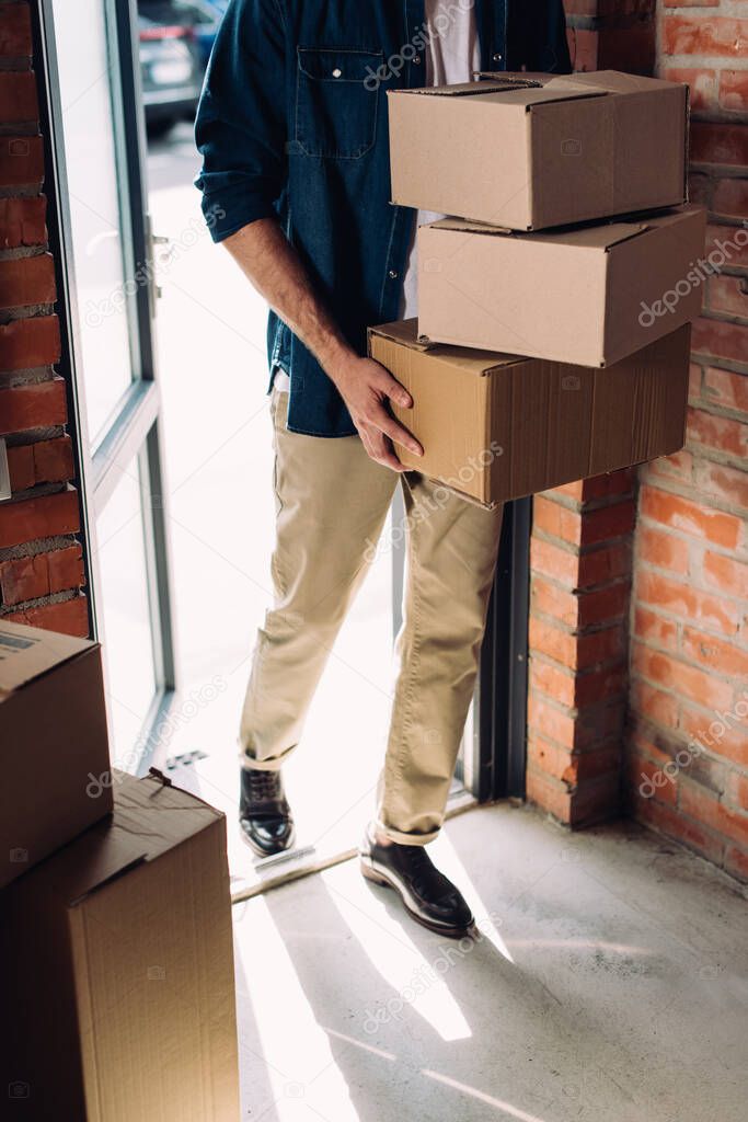 cropped view of businessman holding carton boxes while walking in new office 
