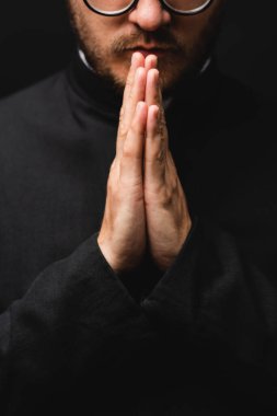 partial view of bearded priest with praying hands isolated on black  clipart