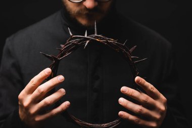 selective focus of priest holding wreath with spikes in hands isolated on black  clipart