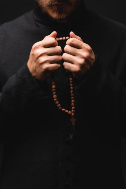 cropped view of priest holding rosary beads in hands isolated on black  clipart
