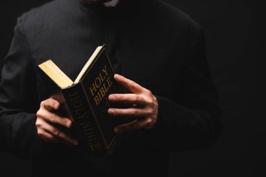 partial view of pastor holding holy bible in hands isolated on black  clipart