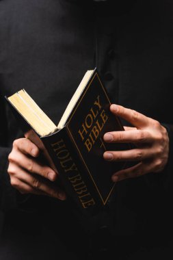 partial view of pastor reading holy bible isolated on black  clipart