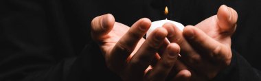 horizontal crop of priest holding burning candle isolated on black  clipart