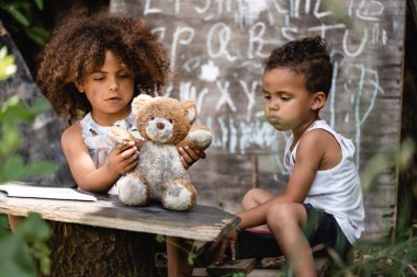 Zavallı Afrikalı Amerikalı çocuğun seçici odak noktası. Kardeşinin yanında kirli oyuncak ayıyla oynuyor.