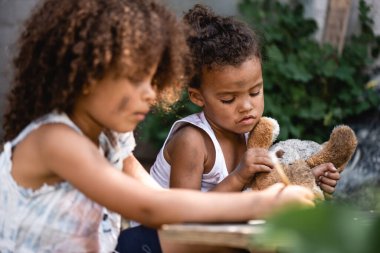 Afrika kökenli Amerikalı bir çocuğun oyuncak ayıyı kız kardeşinin yanında tutup dışarıda yazmasının seçici odağı.