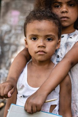 Üzgün Afro-Amerikalı çocuk kalem tutuyor ve zavallı kardeşine sarılıyor. 