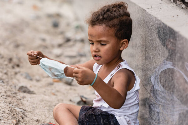 poor african american boy holding dirty medical mask outside