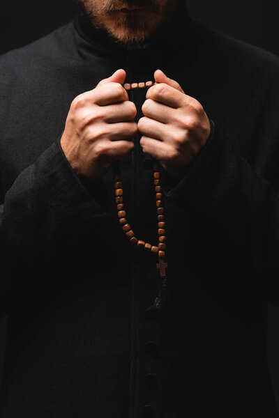 cropped view of priest holding rosary beads in hands isolated on black 