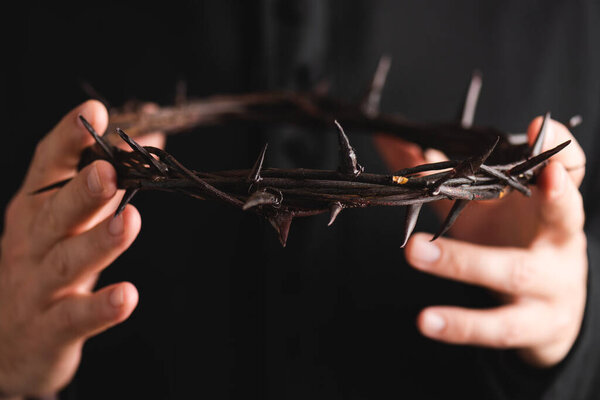 Закрыть священника, держащего острый венок с шипами, изолированными на черном 