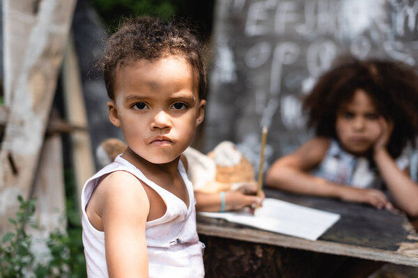 selective focus of poor african american boy looking at camera near curly sister 