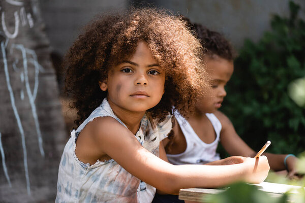 selective focus of african american kid holding pencil near brother sitting outside