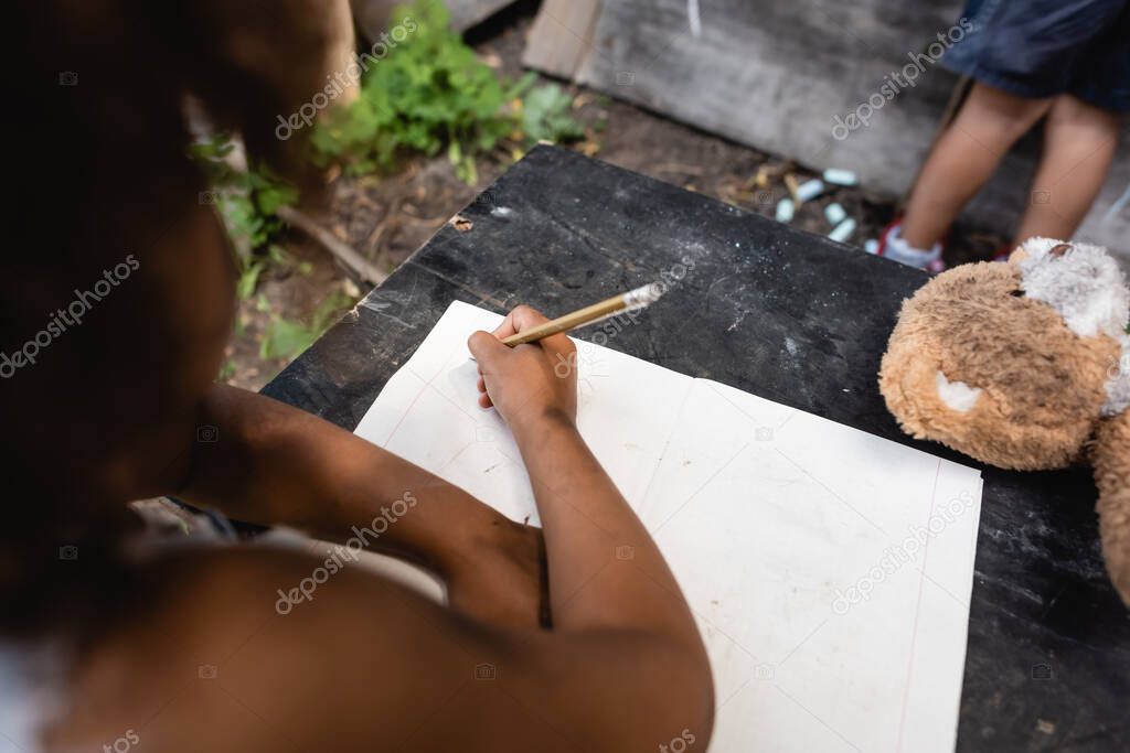 partial view of african american kid holding pencil while writing near child 