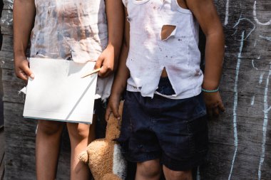 Yırtık elbiseli zavallı Afro-Amerikan çocuğun elinde boş bir defterle duruşu. 