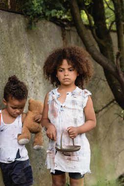 Metal plakalı ve varoşlarda duran kirli oyuncak ayılı Afro-Amerikalı çocuklar. 