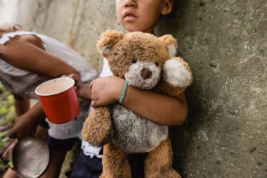 Gecekondu mahallesinde kirli oyuncak ayıyla dilenen evsiz Afro-Amerikan çocukları. 