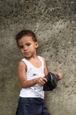 Dilenci Afrikalı Amerikalı çocuk, şehir sokağında beton duvarın yanında cüzdan tutuyor. 