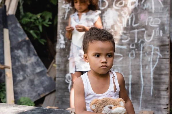 贫穷的非洲裔美国儿童穿着撕破的衣服 坐在黑板和妹妹旁边的软玩具上 有选择地集中注意力 — 图库照片