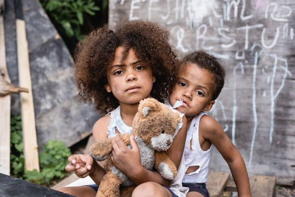 poor african american kids with dirty teddy bear looking at camera