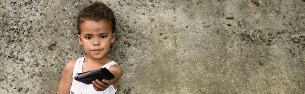在城市街道混凝土墙边拿着钱包的非洲裔美国儿童全景照 — 图库照片