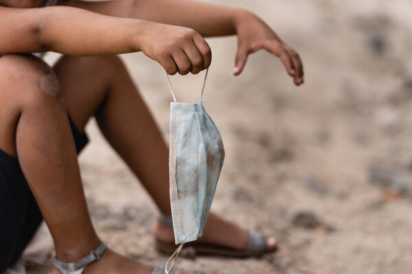Cropped view of african american kid holding dirty medical mask on urban street 