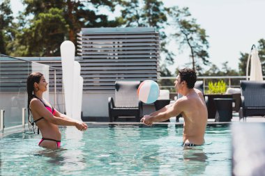 happy couple playing volleyball with inflatable ball in swimming pool 