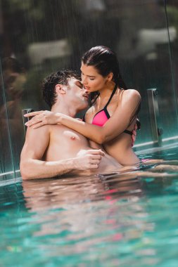 Havuzda ıslak kızla kucaklaşan seksi adam. 