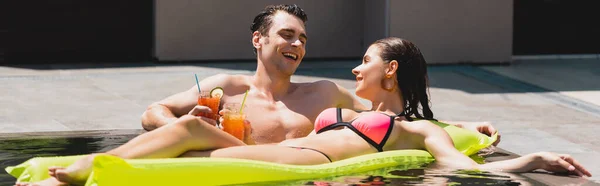 幸せな女性のパノラマ作物プールでカクテルを保持陽気な男の近くにインフレータブルマットレスに横たわっている — ストック写真