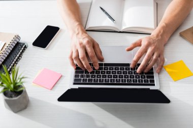 Evdeki masada boş ekranlı ve akıllı telefonlu bir adamın dizüstü bilgisayarda yazışının en üst görüntüsü, çevrimiçi konsept kazanma