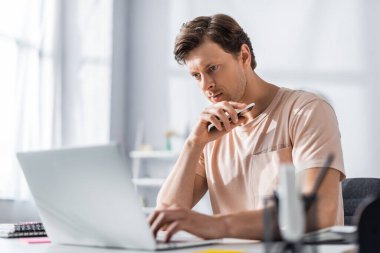 Bilgisayara bakan ve masada oturup online konsept kazanırken cep telefonu tutan yakışıklı tele-işçilerin seçici odak noktası