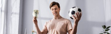 Evde para ve futbol oynayan pozitif bir adamın panoramik mahsulü 