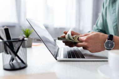 Bilgisayarın yanında dolar banknotları sayan bir adam manzarası ve masada bir fincan kahve, online konsept kazanç
