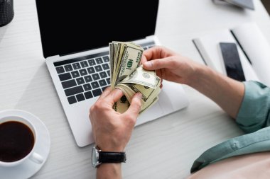 Masada boş ekranları olan kahve fincanının yanında dolar banknotları tutan ve online konsept kazanan bir adamın görüntüsü.