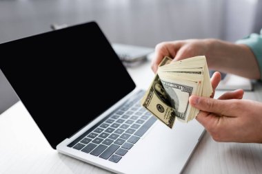 Bilgisayarın yanında dolar banknotları tutan, boş ekranlı, online konsept kazanan bir adamın görüntüsü.