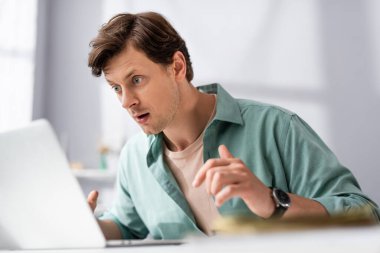 Selective focus of shocked teleworker looking at laptop at home, earning online concept clipart