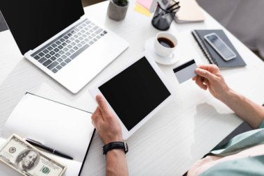 Adamın elinde kredi kartı ve dijital tablet olan, doların yanında boş ekran ve masada bir defter tutan, online konsept kazanan bir adam görüntüsü.