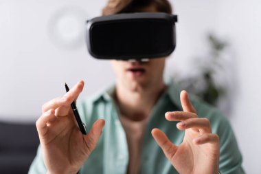 Selective focus of man in vr headset holding pen at home  clipart