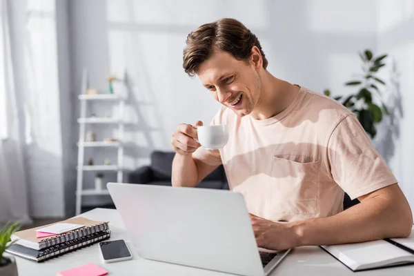 Lächelnder Mann Schaut Auf Laptop Bildschirm Und Hält Tasse Neben — Stockfoto