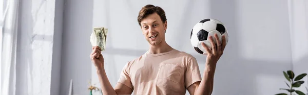 Panoramic crop of positive man holding money and football at home 