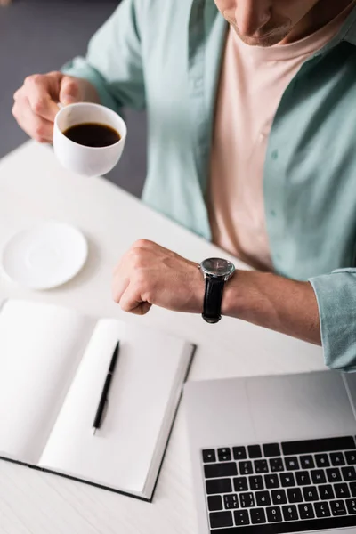 프리랜서가 노트북과 노트북 근처에서 커피를 마시는 손목시계에 시간을 확인하는 — 스톡 사진