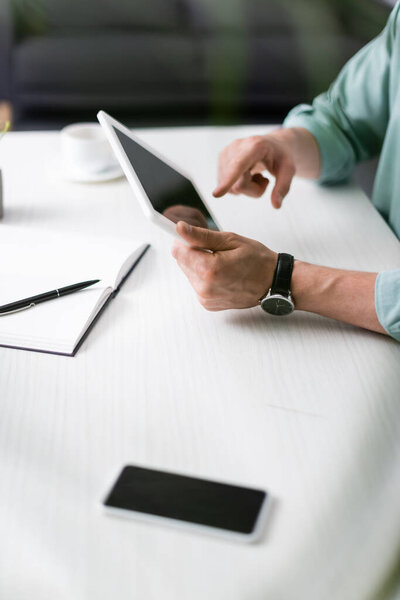 Cropped view of man using digital tablet beside smartphone and notebook on table, earning online concept