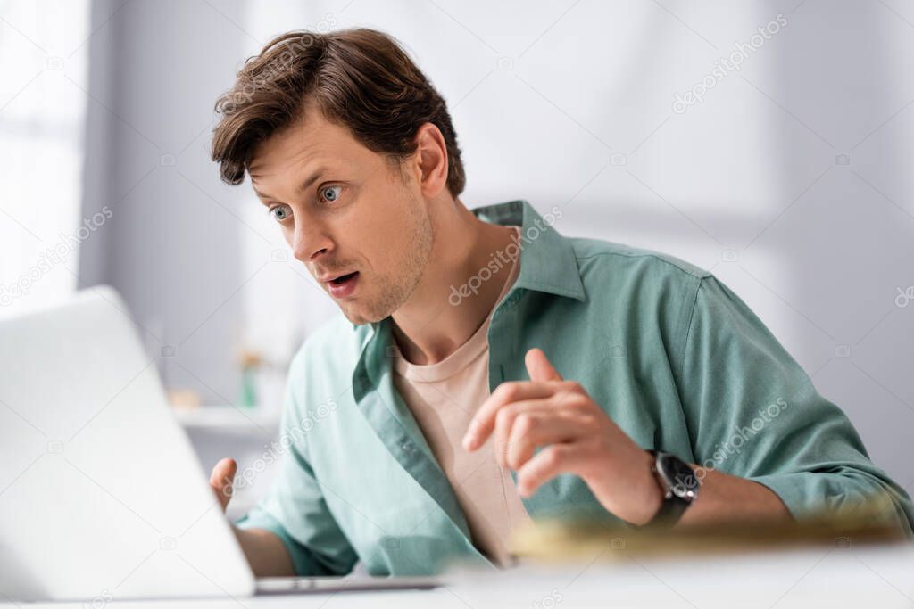 Selective focus of shocked teleworker looking at laptop at home, earning online concept