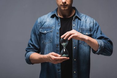 Cropped view of man holding hourglass on grey background, concept of time management  clipart