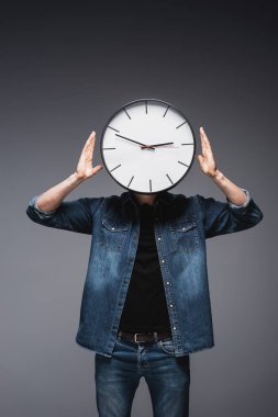 Young man in jeans jacket with clock on head on grey background, concept of time management  clipart
