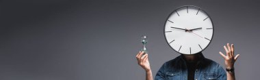 Panoramic shot of man with clock on head holding hourglass and gesturing on grey background, concept of time management  clipart