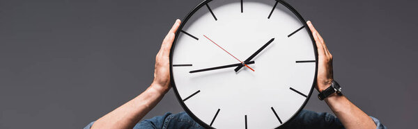 Панорамный урожай человека, держащего часы у лица изолированные по серому, концепция управления временем 