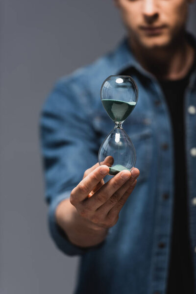 Cropped view of young man holding hourglass isolated on grey, concept of time management 