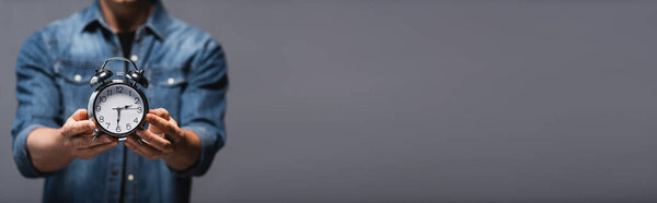 Панорамная ориентация человека, показывающего будильник, изолированный на сером с копировальным пространством, концепция управления временем 