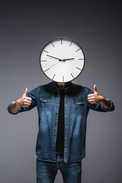 Man with clock near face showing thumbs up on grey background, concept of time management 