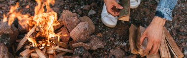 panoramic concept of man touching wooden log near burning bonfire clipart