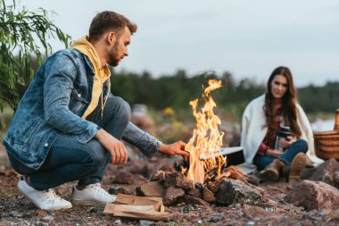 selective focus of man sitting near burning bonfire and girl   clipart